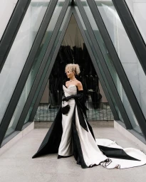 Woman in an elegant white and black gown with a long train posing inside a triangular glass architectural frame