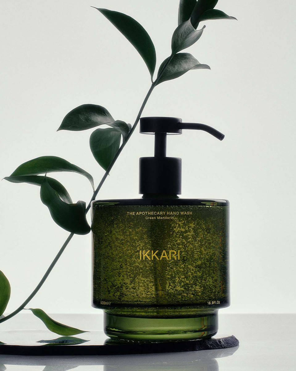 Still life shot of a green glass bottle of Ikkari Apothecary Hand Wash with a black pump, staged with a leafy green branch.