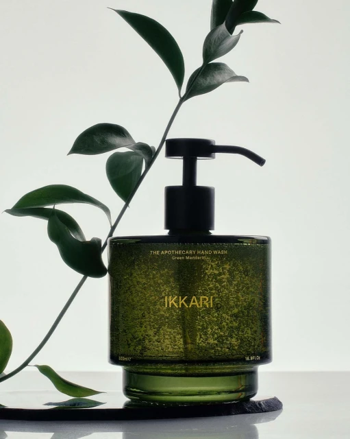 Still life shot of a green glass bottle of Ikkari Apothecary Hand Wash with a black pump, staged with a leafy green branch.