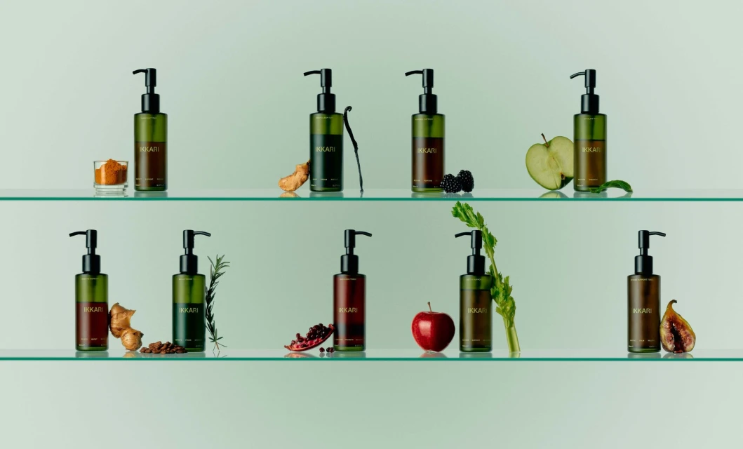 Bottles of Ikari product displayed on glass shelves with fruit, vegetables, and spices against a soft green gradient background.