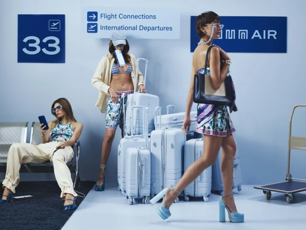 Three fashionable women in an airport terminal with luggage, wearing stylish outfits and accessories, waiting near gate 33.