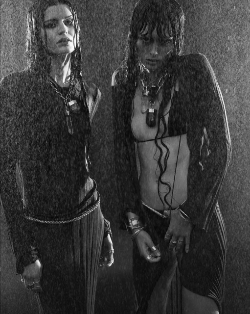 Two women in black outfits stand in the rain, showcasing dark fashion and dramatic beauty. Shot in a grayscale aesthetic.