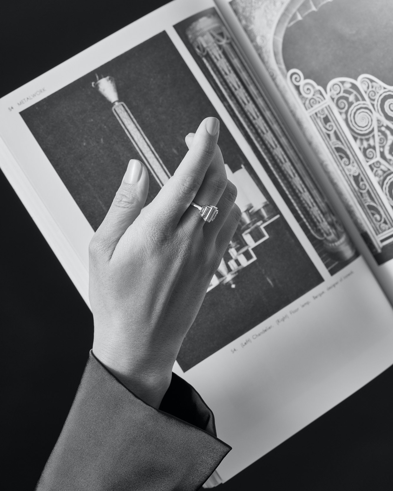 Close-up shot of a hand wearing a ring, placed on an open magazine displaying monochrome architectural photographs on its pages.