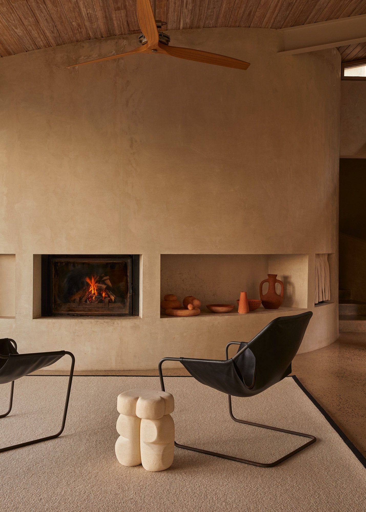 Contemporary interior with two black sling chairs, a white side table, and a fireplace set within a beige stucco wall.