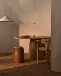 Minimalist interior with a round wooden dining table, wooden chairs, a floor lamp, and a textured neutral wall background.