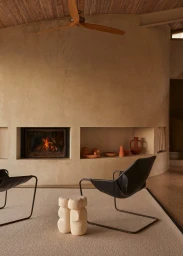 Modern interior living room featuring a fireplace, black leather armchairs, a wooden ceiling fan, and ceramic decor.