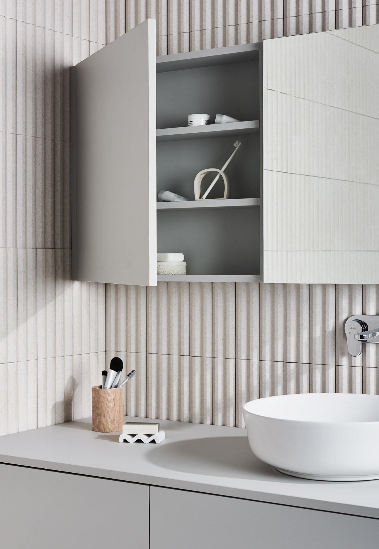 Bathroom interior featuring a white vessel sink, grey vanity, and open medicine cabinet with bathroom supplies against a textured wall.