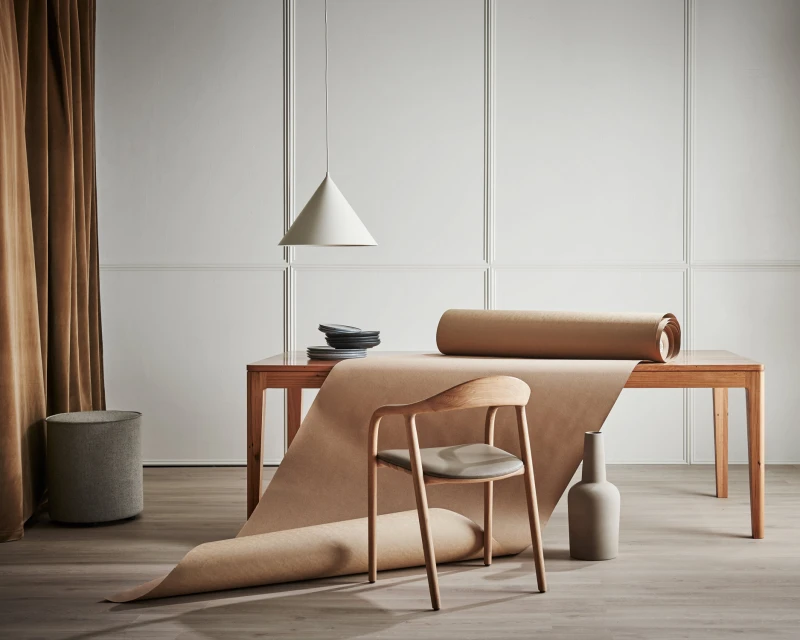 Minimalist interior featuring a wooden chair, table, pendant lamp, and decorative objects against a neutral backdrop with warm brown accents.