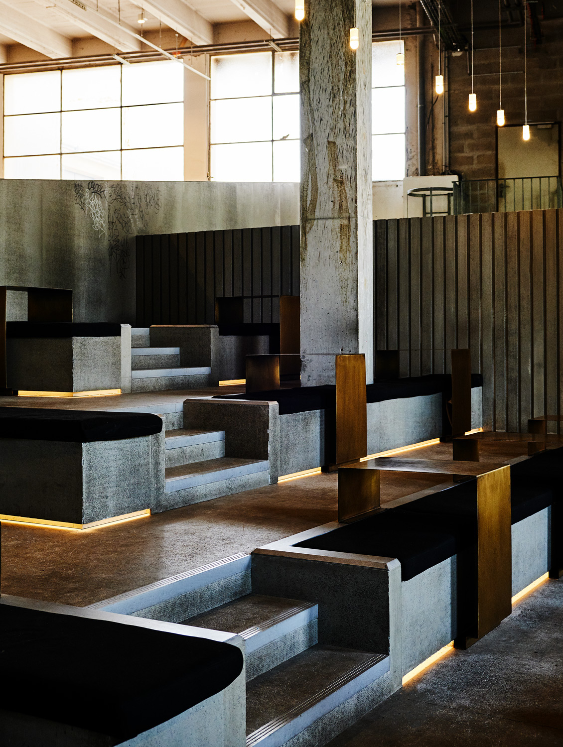 Interior of a room with concrete steps and cushioned seating, accented by warm lighting, creating an inviting architectural space.