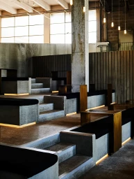Modern interior architecture featuring tiered concrete seating with integrated warm LED strip lighting and vertical wooden paneling.