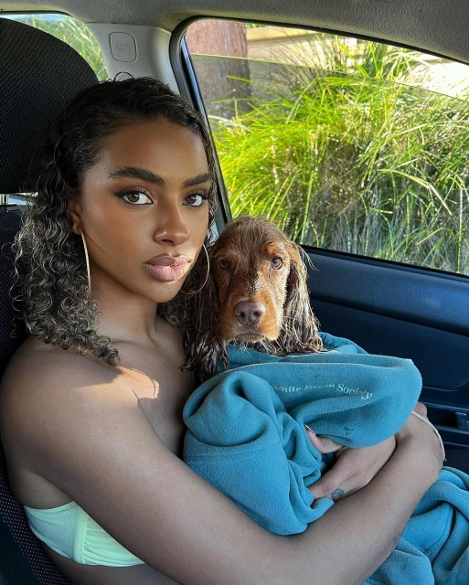 Young woman holds a Spaniel dog wrapped in a turquoise towel while sitting in a car, highlighting a heartwarming and intimate scene.