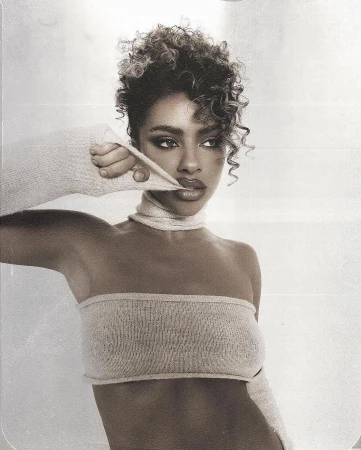 Portrait of an adult female model with curly hair wearing a beige strapless top and scarf, striking a fashionable pose in a photo studio.