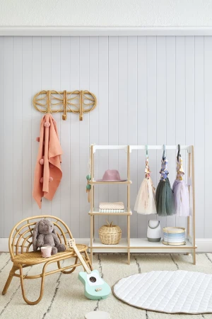 Rattan furniture and playful decor in a children's room with a wooden clothing rack, toy guitar, stuffed animal, and soft neutral colors.
