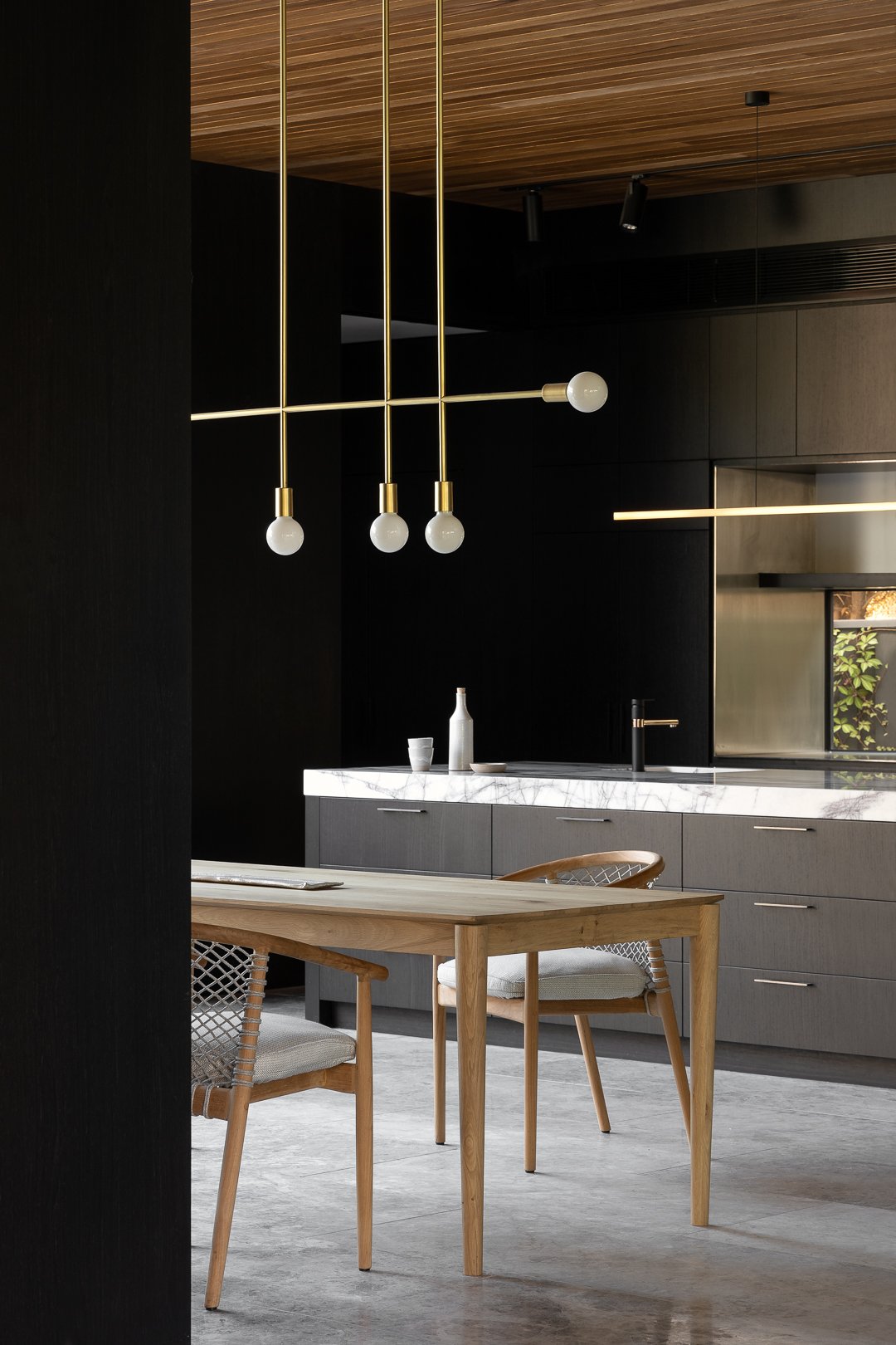 Contemporary kitchen and dining space featuring a wooden table with woven chairs, a modern chandelier, and sleek gray cabinets.