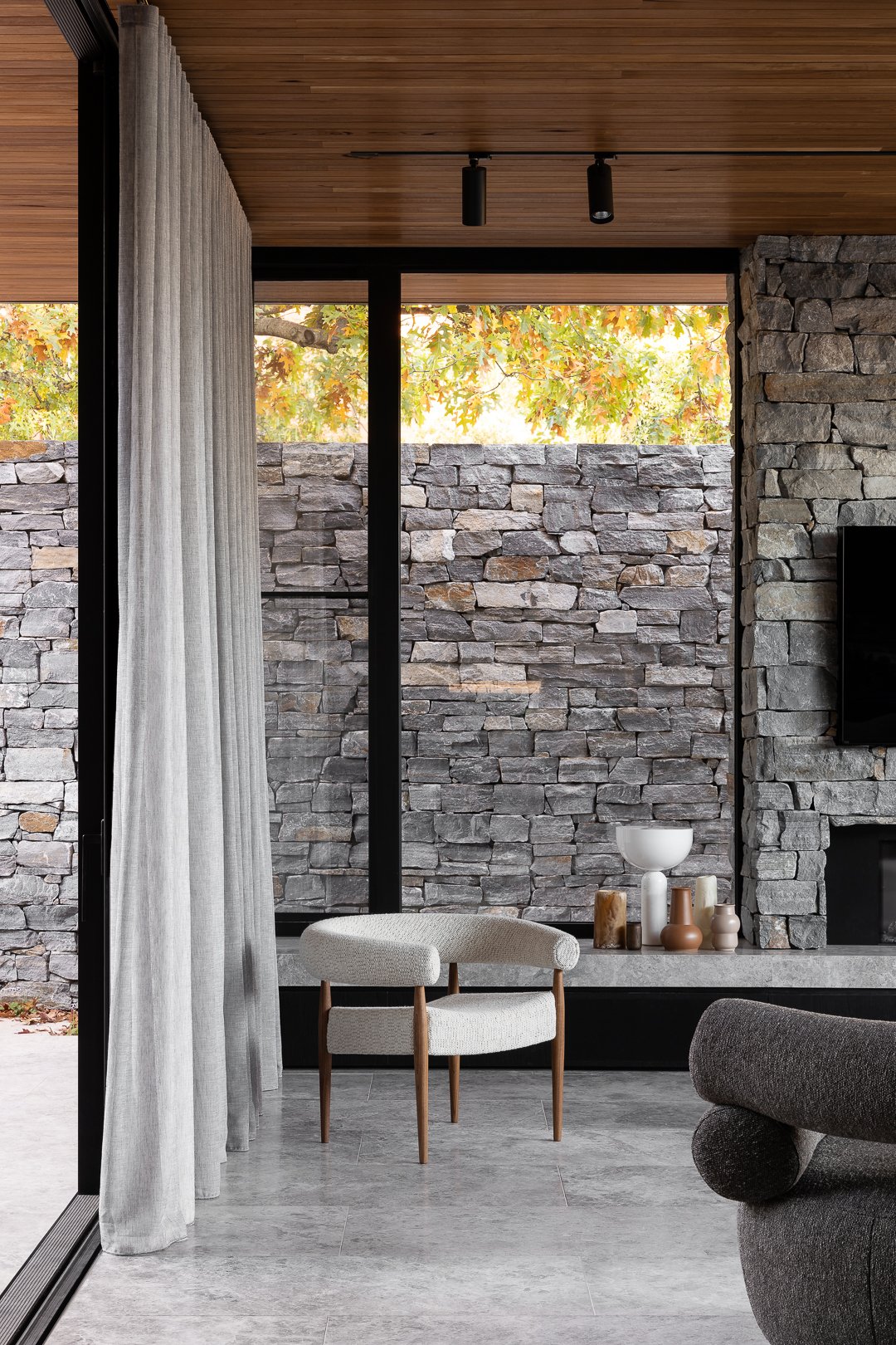 Interior view of a modern living room featuring a stone wall, a white chair, and sheer curtains for a minimalist, elegant design aesthetic.