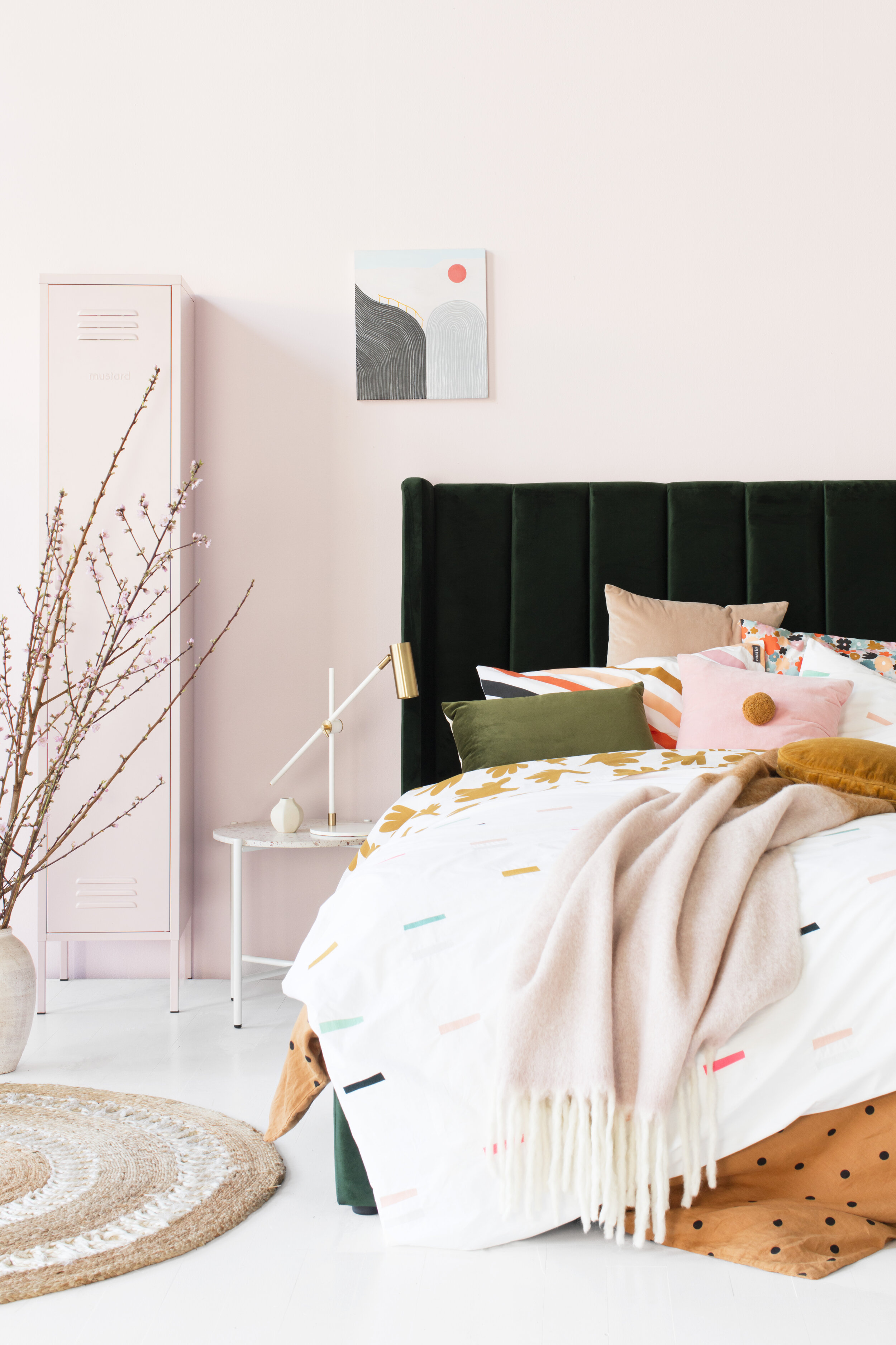 Modern bedroom interior showcasing a bed with colorful pillows and blankets, set against a pink wall with decorative accents.