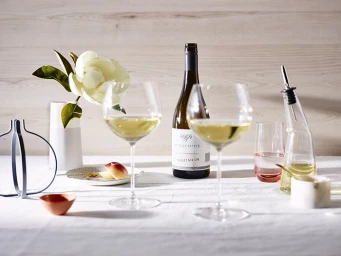 Wine bottle and two filled wine glasses on a linen-covered table with a white flower in a vase
