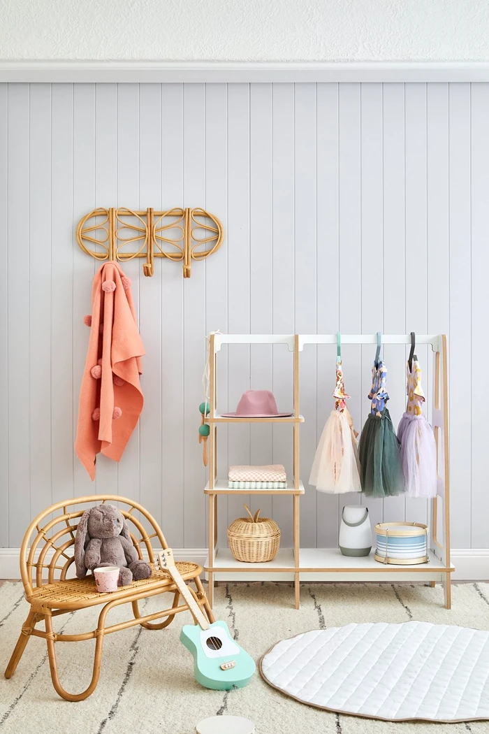 Childrens wooden clothing rack and rattan bench with plush toy against a pale vertical panel wall