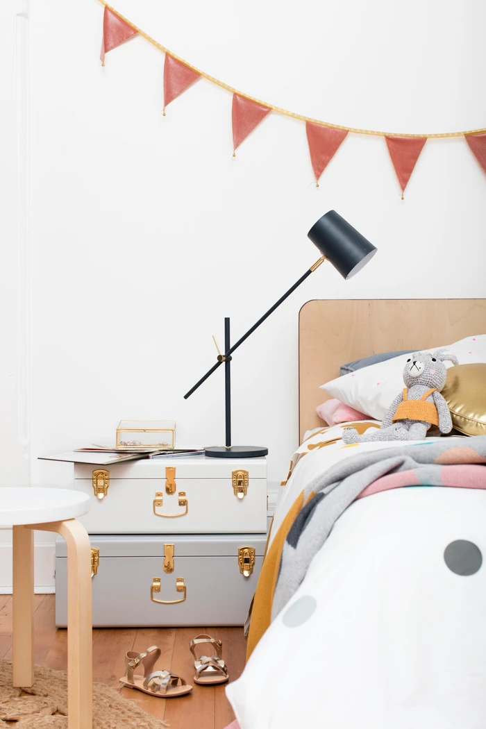 Children bedroom interior styled by Madeline Mcfarlane featuring stacked storage trunks and a modern black desk lamp.