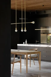 Modern interior kitchen and dining space featuring a wooden table, brass pendant lights, and dark cabinetry styled by Madeline Mcfarlane