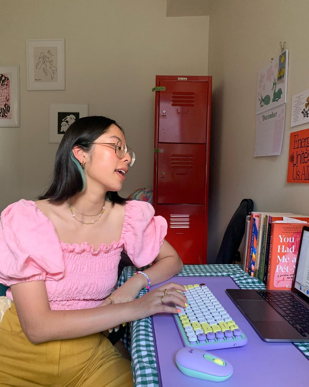 Woman in pink top typing on a keyboard at a lilac desk, indoor setting, with a red locker visible in the background.