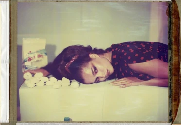 Woman in red and black polka dot dress reclining on a white surface with small white objects and a bag.