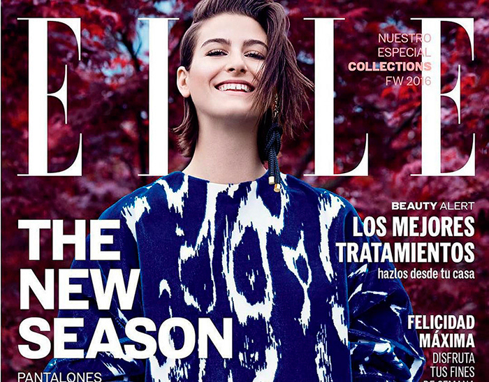 Elle magazine cover featuring a smiling adult woman wearing an abstract-patterned shirt, against a blurred, reddish-purple floral background.