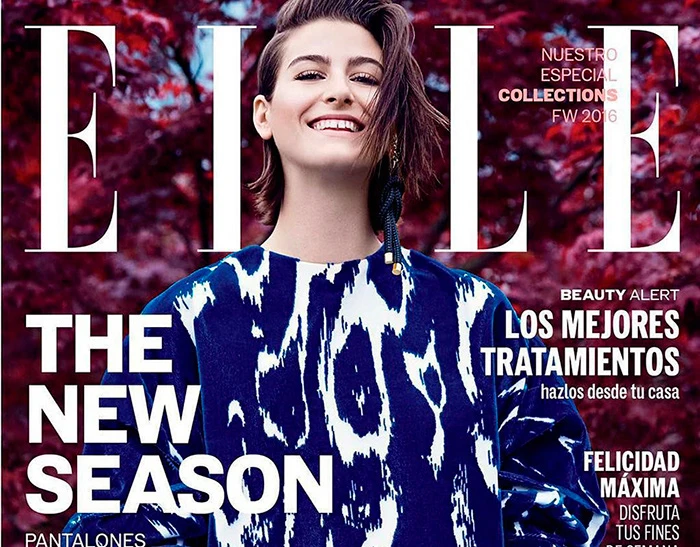Elle magazine cover featuring a smiling adult woman wearing an abstract-patterned shirt, against a blurred, reddish-purple floral background.