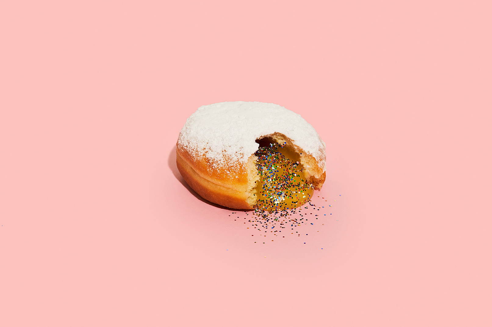 Powdered donut filled with gold glitter on a pink background. Confectionary dessert treat concept. Food photography. Still life.