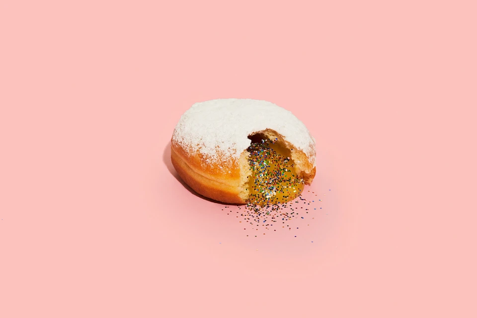 Powdered donut filled with gold glitter on a pink background. Confectionary dessert treat concept. Food photography. Still life.