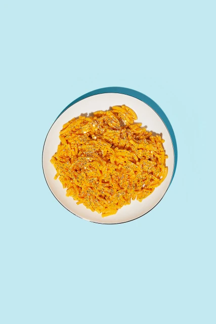 Overhead shot of macaroni and cheese served on a white plate against a bright blue background, creating a colorful and appetizing image.
