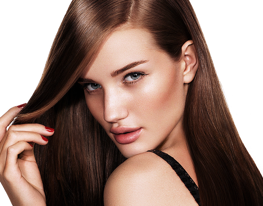 Close-up shot of a stunning woman with sleek brown hair, clear blue eyes, flawless skin, and red nails, against a clean white background.