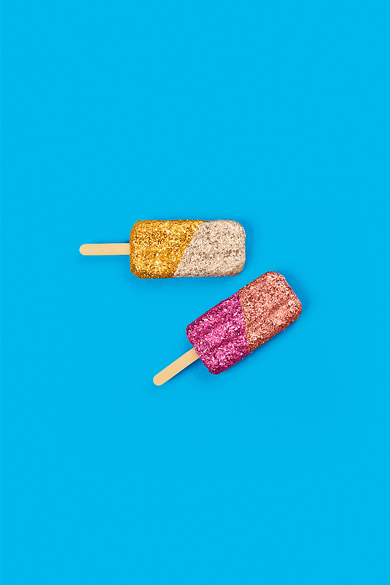 Two colorful glittered ice pops on a vibrant blue background create a fun, eye-catching image perfect for summer or sweet treat themes.