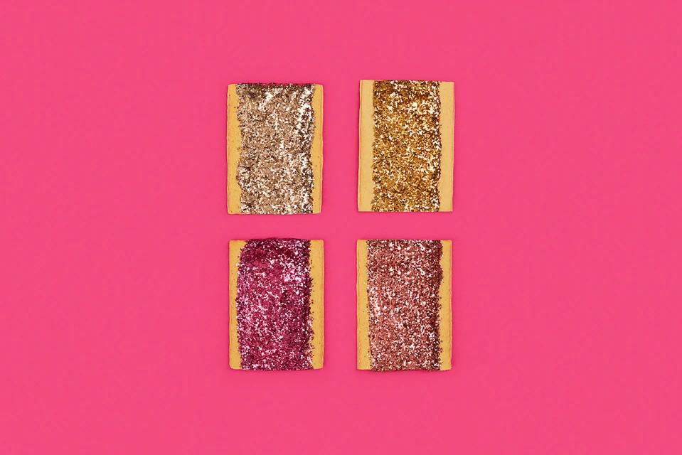Four rectangular treats covered in glitter on a vivid pink background, arranged in a square pattern, creating a visually striking composition.
