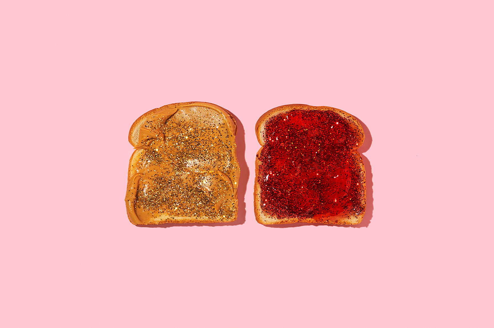 Two slices of toast are side-by-side on a pink background, one with peanut butter and gold glitter and the other with red jam and red glitter.