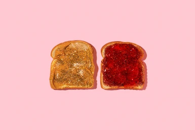 Two slices of toasted bread, one spread with peanut butter and one with jelly, resting side by side on a solid pink background.