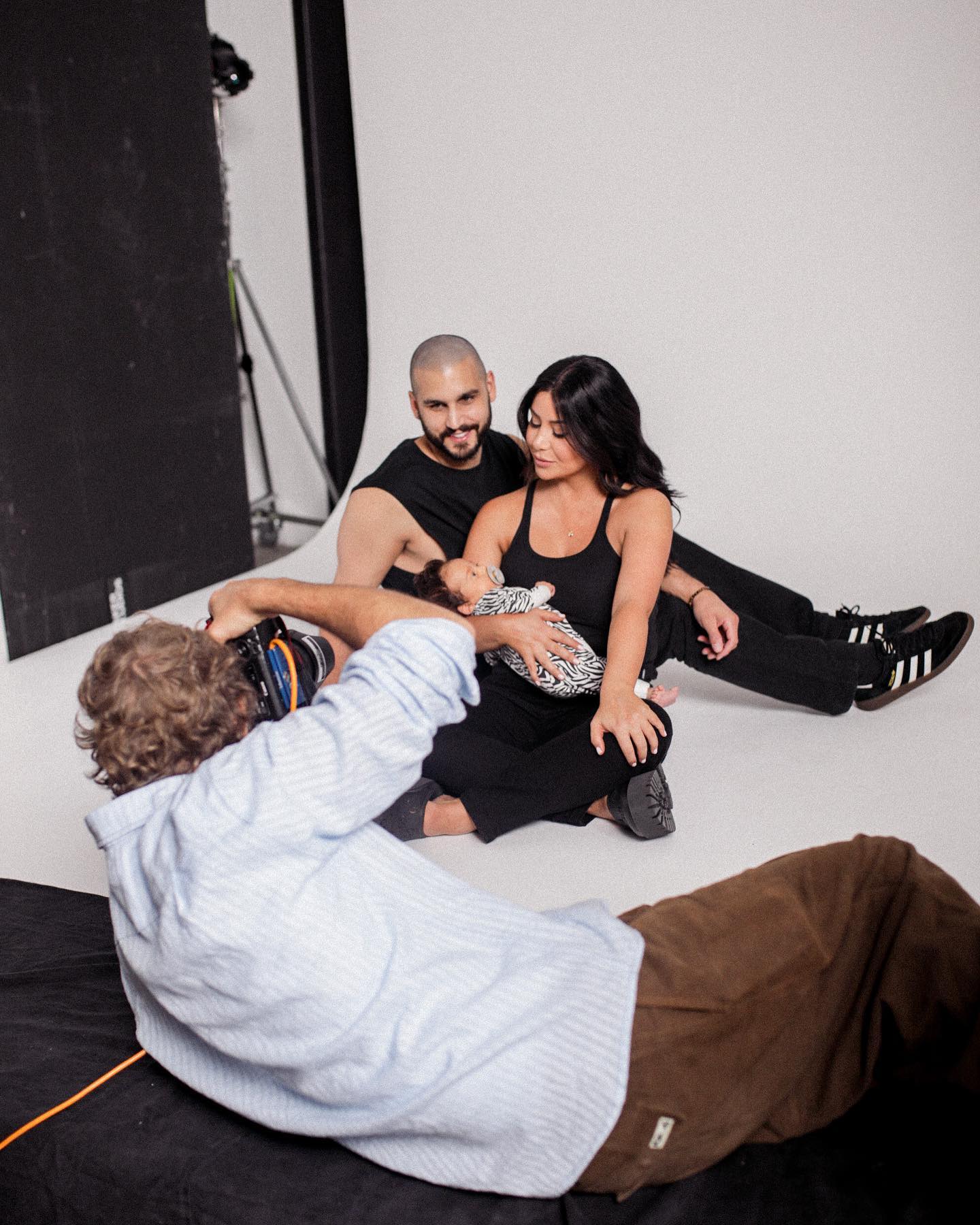 Family portrait in photo studio: Father, mother, and baby are posing while a photographer kneels to capture the shot.