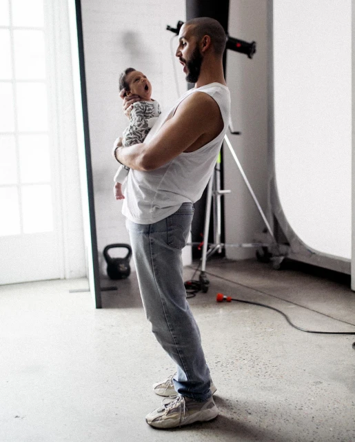 Father holding a yawning baby in photo studio with lighting equipment and white background for a family portrait or lifestyle shoot.