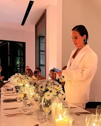 Martha Kalifatidis wearing a white blazer giving a speech at a candlelit dinner table with floral centerpieces in Sydney