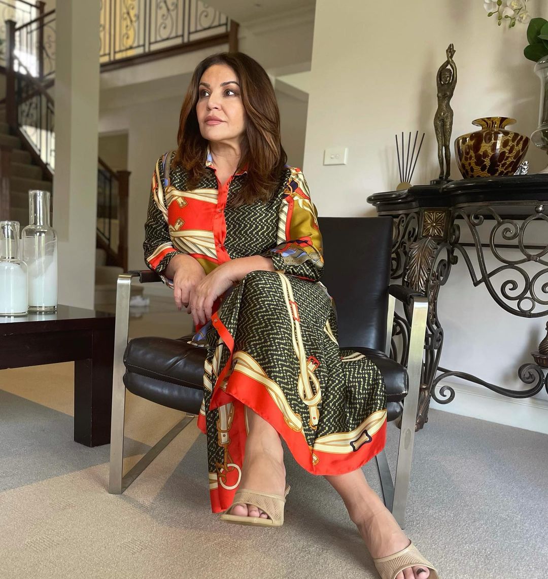 Woman in patterned shirt dress sitting in leather chair indoors with neutral carpet, table and home decor in the background.