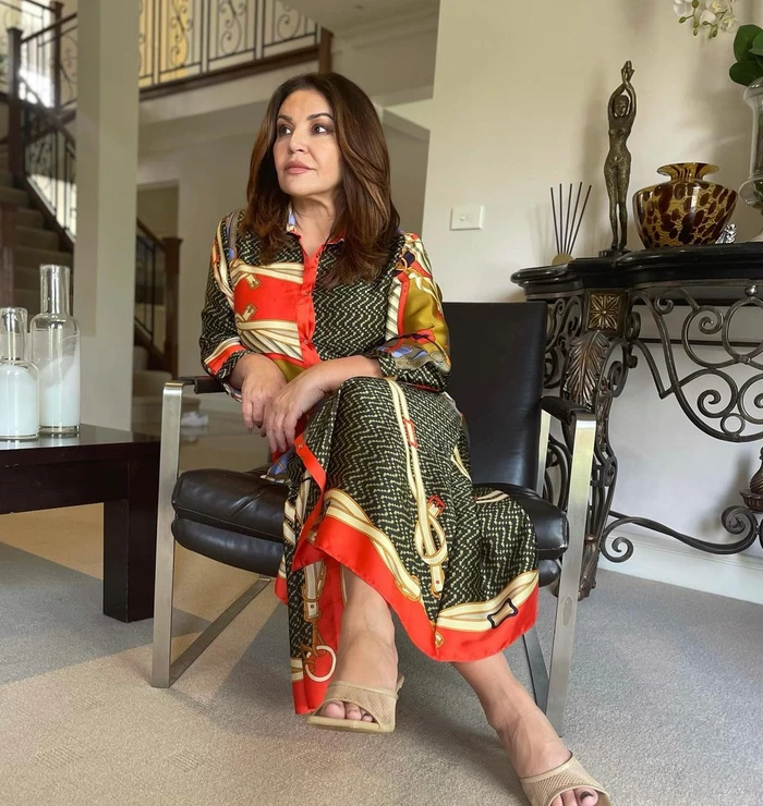 Woman in patterned red and green silk dress seated on a black leather chair inside a home interior