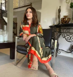 Woman in patterned red and green silk dress seated on a black leather chair inside a home interior