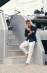 Smiling man in dark blue shirt and white trousers leaning against a modern yacht staircase in Sydney