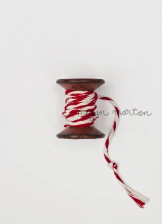 Wooden spool with red and white twine on a white surface, showcasing crafting and decorative supplies with a simple, clean aesthetic.