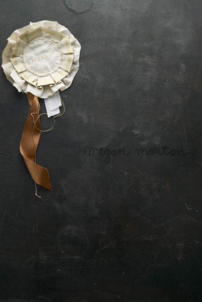 Rosette ribbon with satin streamer against a textured dark grey background with cursive handwriting, evoking a vintage or crafted aesthetic.