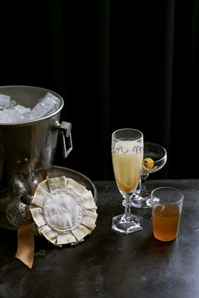 Celebratory still life with crystal glasses, silver ice bucket filled with ice, and a white rosette on a dark metallic table.