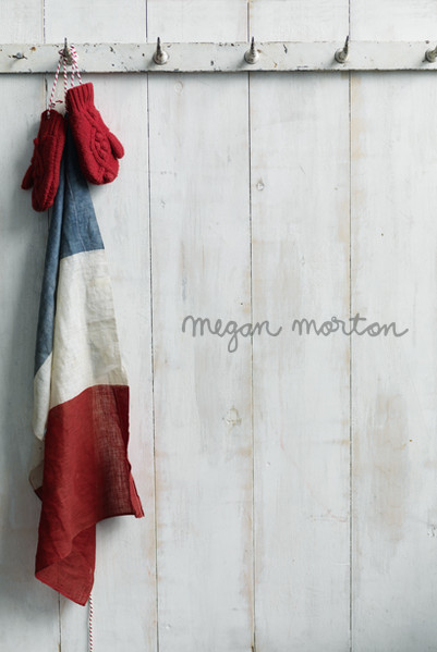 Red mittens and a striped cloth hanging from a rustic coat rack against a weathered white wall, creating a cozy, vintage aesthetic.