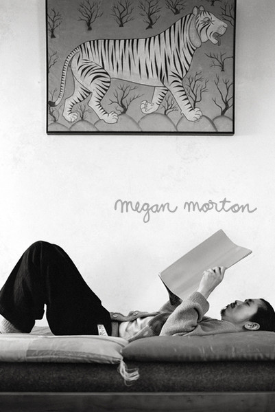 Black and white photo of person reading on chaise lounge below tiger art on wall; relaxed, comfortable, and intimate setting indoors.