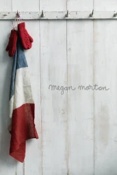Red knit mittens and a tricolor cloth hanging from hooks on a white paneled wooden wall styled by Megan Morton