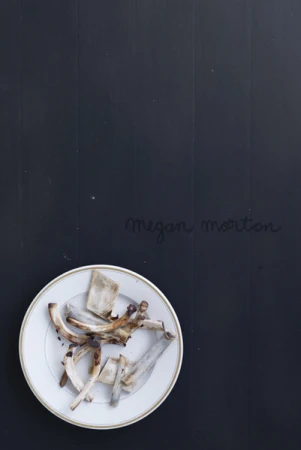 A white plate containing small animal bones sits on a dark wooden surface with handwritten text.